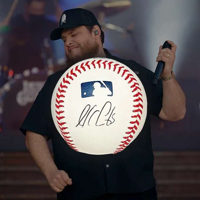 An MLB baseball signed by Luke Combs in front of a photo of Luke Combs performing.
