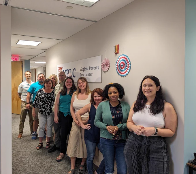 VPLC staff stand in front of a sign with the VPLC logo and colorful folded paper wall decorations