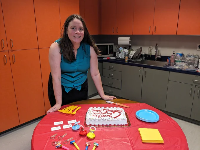 Virginia Hunger Solutions director Cassie Edner stands in front of a table with a cake and party decorations