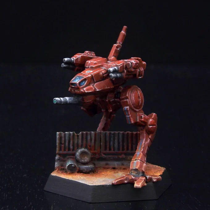 A painted miniature of a Locust 'Mech.  It is dull red with a few thin blue stripes as accents.  It is standing over a length of rusted metal fencing.
