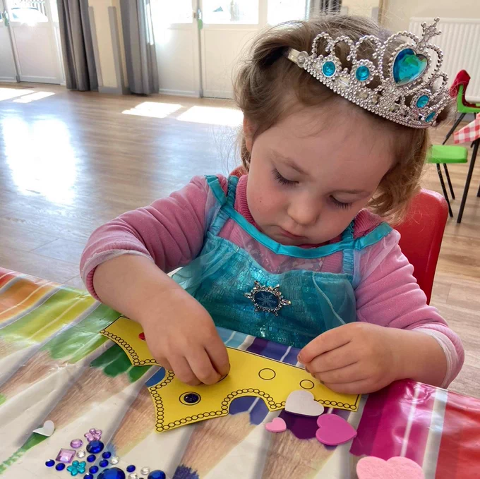 A child being creative making a paper crown with coloured jewels to wear. 