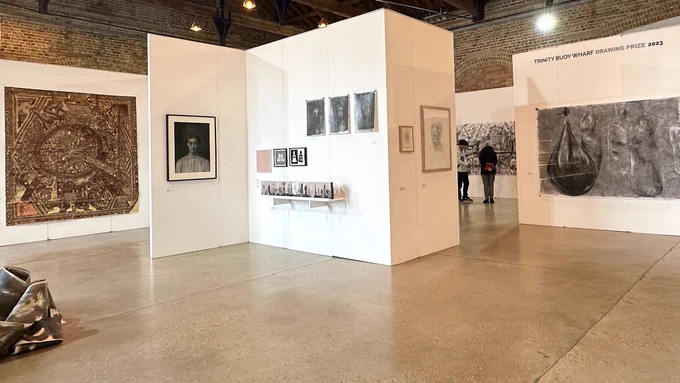 The exhibition space of the Trinity Buoy Wharf Drawing Prize 2023 - a number of drawings are hung on white walls, all different in their colour and size