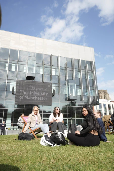 Students sitting on grass with a screen in the background that reads 200 years of the University of Manchester