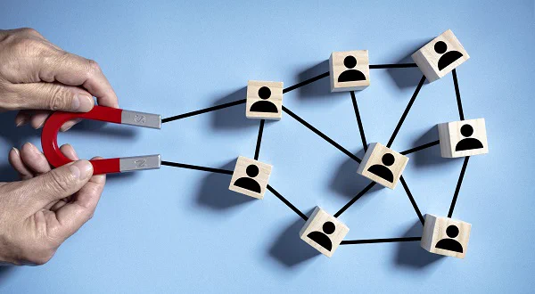 Two hands hold a magnet, which has black lines connecting it to small wooden boxes with people icons on. 