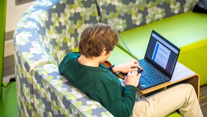 Student sitting on patterned green couch on laptop.