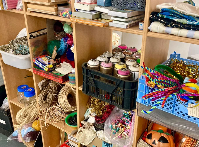 Shelving unit filled with colourful art materials including fabrics, spray paint yarn and trims.