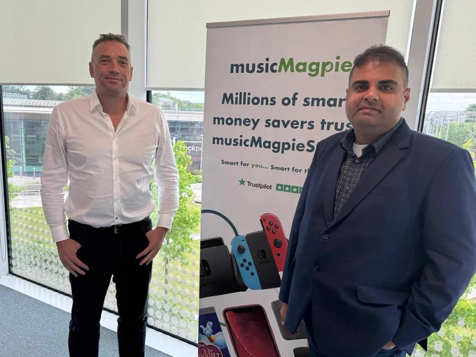 Navendu Mishra with the managing director of musicMagpie, in front of a banner with the company logo.