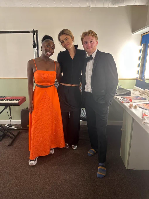 A photo showing three individuals in a dressing room posing for a photo