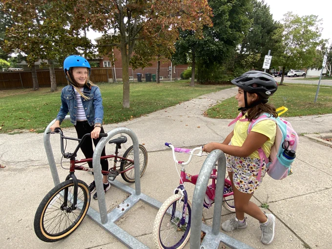 Two students with their bikes at a bike rack.