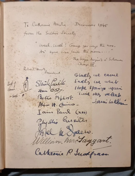 A mottled blank page written on by many people in pencil and ink. It reads:

To Catherine Hastie December 1945 from the Saltire Society
"Weel, weel! Gang yer weys the noo, an' syne come back the morn..."
The Wyse Sayin's o' Solomon Chap[ter] 3.
[signed] Robert Hurd, President.

Then a list of signatures of wellwishers and a motif/emblem/device drawn in ink. It is an oval sat on the centre of a line at an acute angle. What looks like a backward lowercase R in the oval's centre. Two bold dots, one atop the oval, the other below the acute line. 