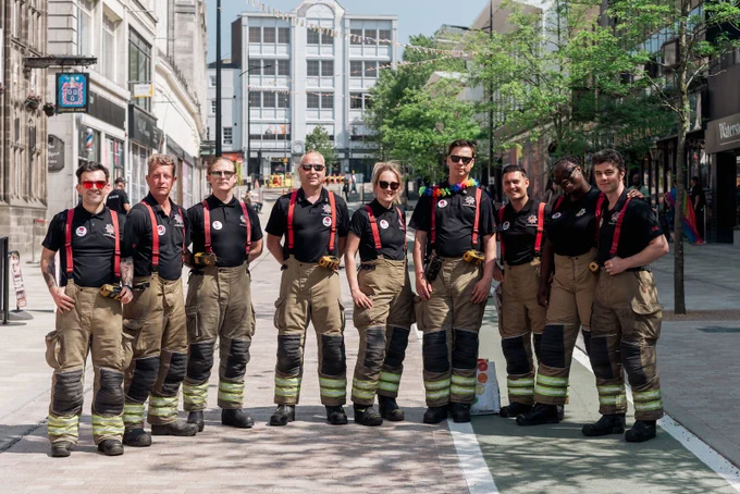 Group of nine West Midlands Fire Service firefighters in uniform posing on a city street during Wolverhampton Pride 2023.