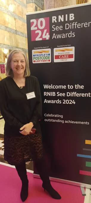 Jane standing by an RNIB #SeeDifferentlyAwards banner at the ceremony in London.