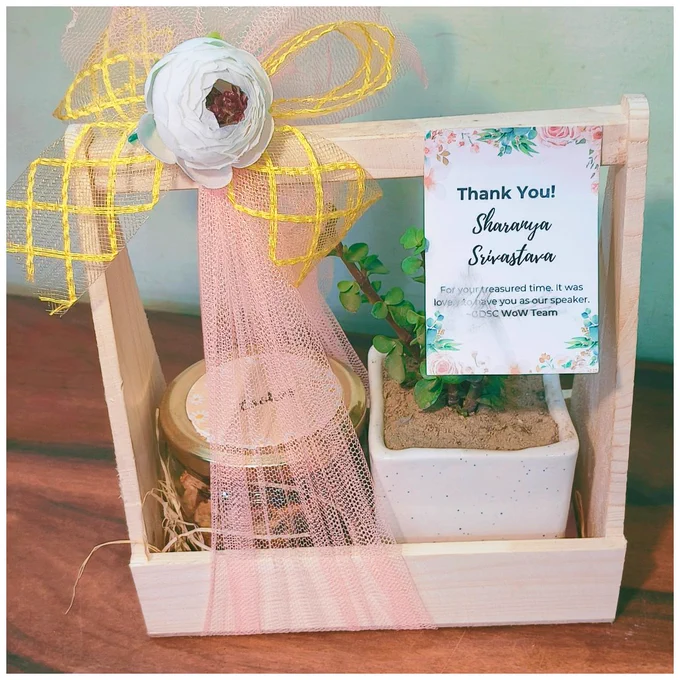The speaker memento including a Jade Plant and Jar of Cookies decorated in a wooden tray with pink and yellow ribbons and a small thank you note attached to it.