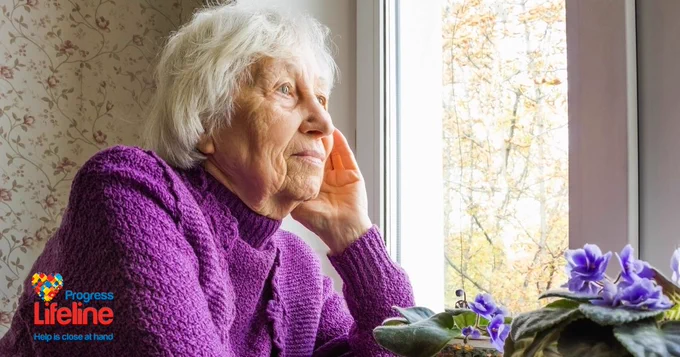 Image of an elderly woman looking out of the window. She is lonely