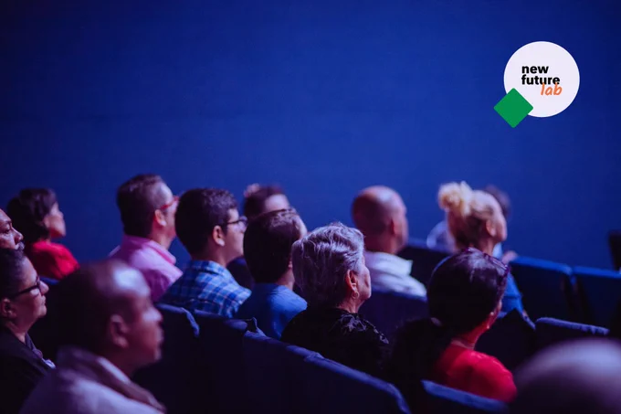 Op de foto zie je een zaal met mensen aandachtig luisteren naar een presentatie.