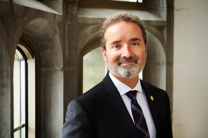 A professional portrait of Dr. Rene Van Acker dressed in a suit in front of an arched, stone window.