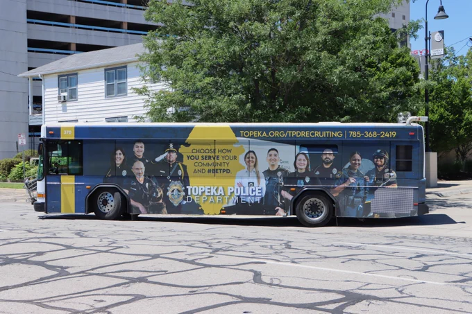 A Topeka Metro bus with a TPD recruitment ad made by Houck Advertising turns south on Monroe St. out of the bus station.