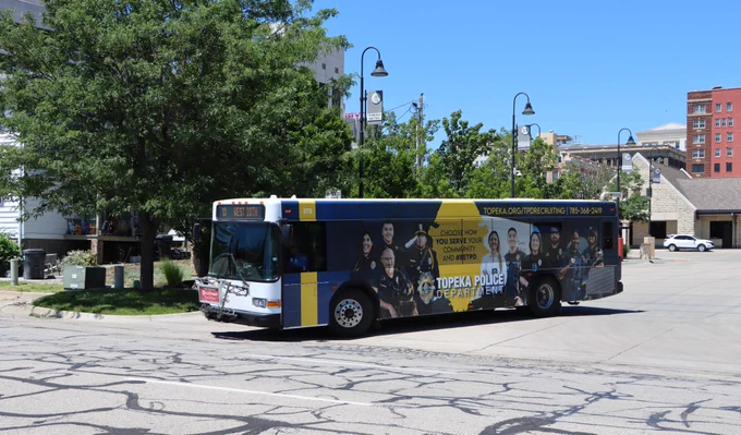 A Topeka Metro bus with a TPD recruitment ad made by Houck Advertising turns south on Monroe St. out of the bus station.