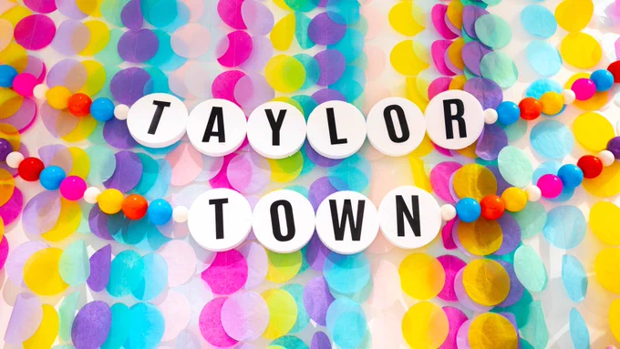 Colourful background covered with multicolored confetti dots, featuring two beaded strings with the words "TAYLOR TOWN" spelled out in white letter beads