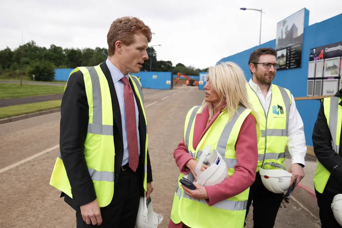 Image shows three people wearing yellow high-vis vests and holding helmets.