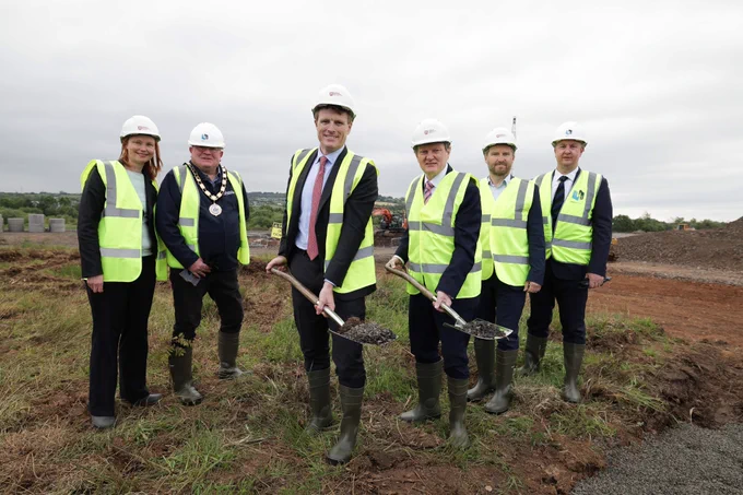 Image shows representatives from industry, government and academia wearing high-vis vests and helmets. Professor Ian Greer and US Envoy Joe Kennedy are pictured in the middle holding shovels.