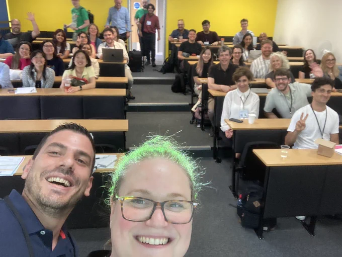 Group selfie of general chairs with attendees. The projector light is shining on Marta’s hair making it look green