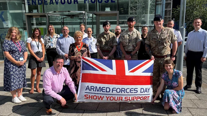 A group of people outside a building holding up the Armed Forces Day flag.
