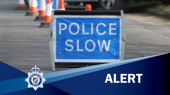 Blue 'Police Slow' sign in road and orange traffic cones in background with the caption 'ALERT'. 