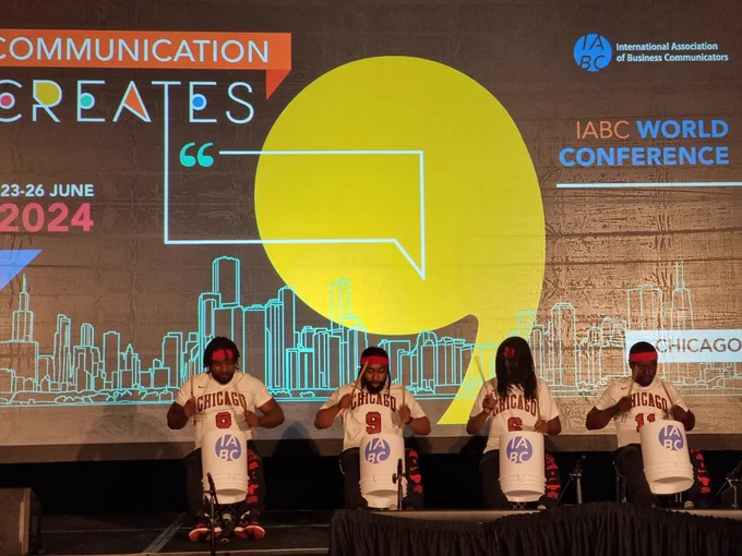 4 men playing IABC-branded bucket drums on the main stage