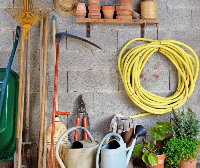 Garden shed with a hose, plant pots, watering cans, and long-handled garden tools. 