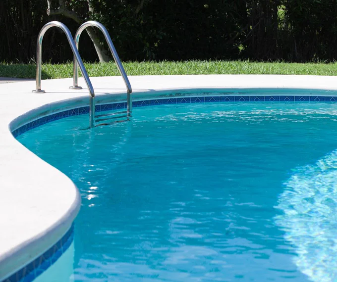 Backyard pool with curved edge and ladder.