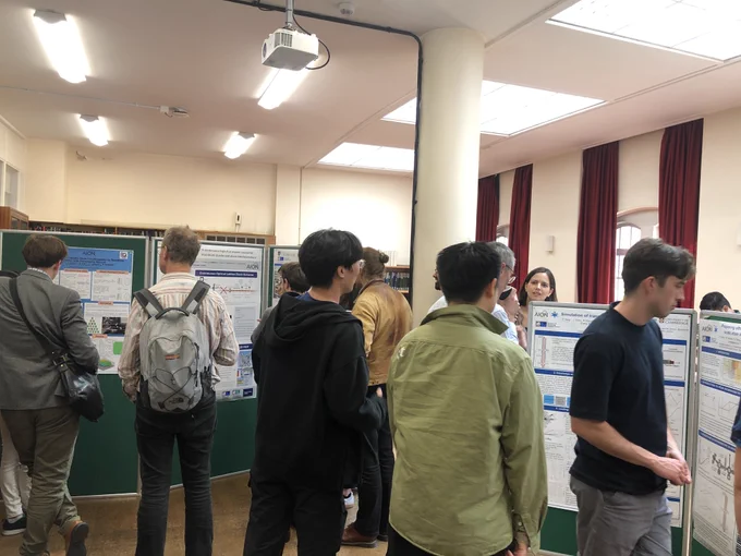 Poster boards have been set up in a large common room, and people are walking around looking at the posters and talking.