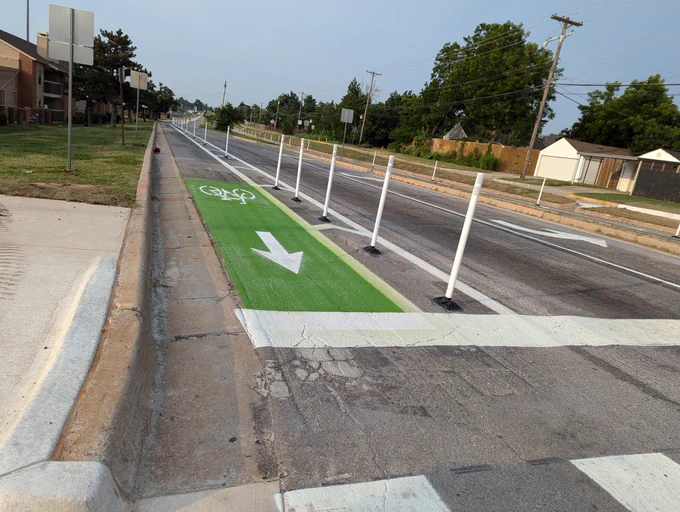 Green painted bike lane with flex post separation, shown near an intersection with fresh crosswalk paint visible.