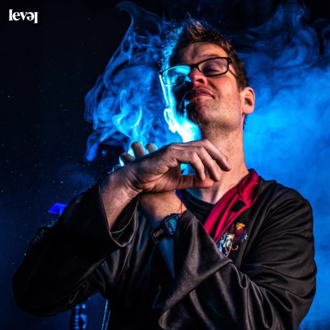 A person dressed in a wizards cloak with blue smoke in the background.