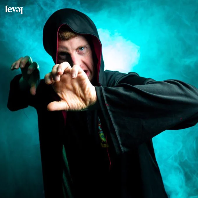 A person dressed in a wizards cloak with turquoise smoke in the background.