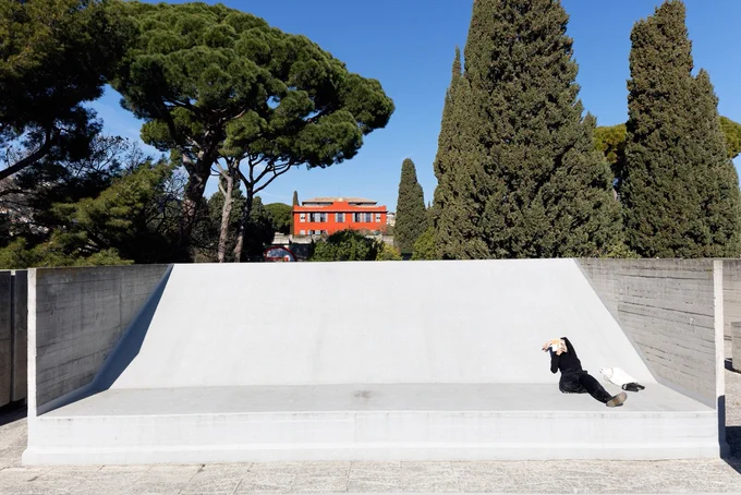 A concrete ramp in a park, with leafy green trees and a bright blue sky