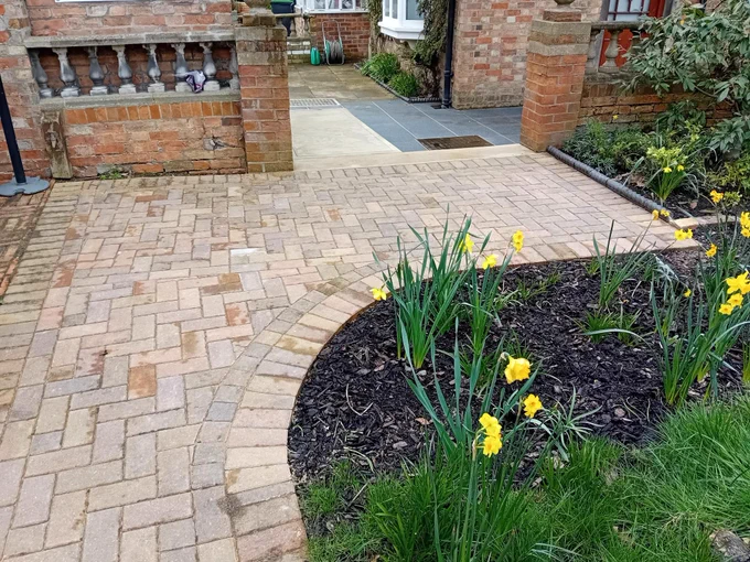 An image of smooth block paving with a ramp in the distance. Nearby are lovely Edwardian brick walls and some daffodills are off to the right. 