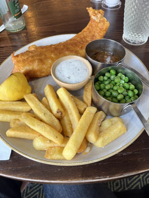 Fried piece of fish, garden peas, thick-cut fries and curry.