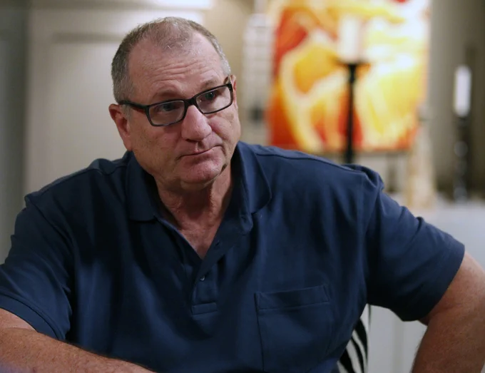 Jay from Modern Family. He is wearing a blue polo t-shirt and glasses. He is sitting at a counter in a home with his right elbow leaning on the surface. He has a disappointed expression 