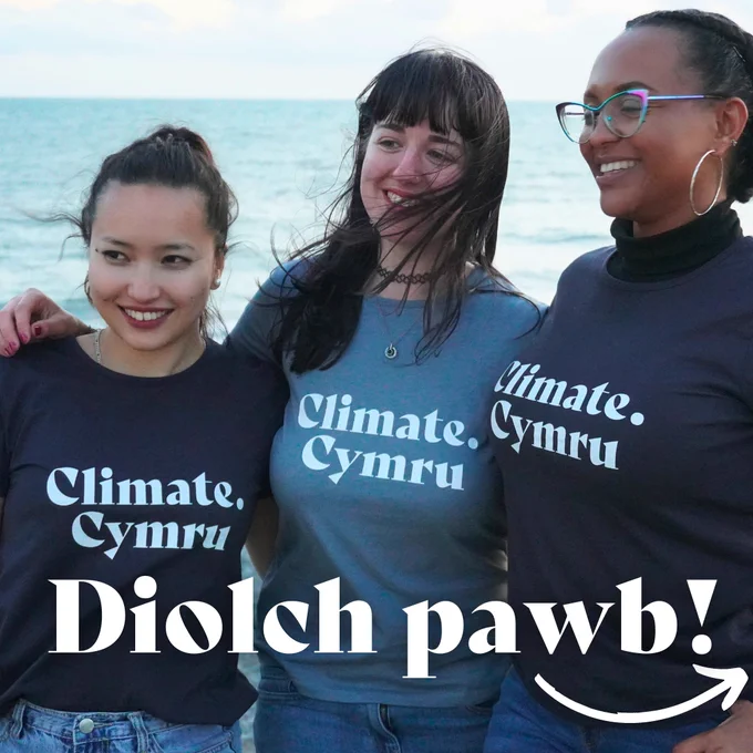3 young women with navy blue tshirts with 'Climate Cymru' printed on the front. Happy and smiling in front of the ocean