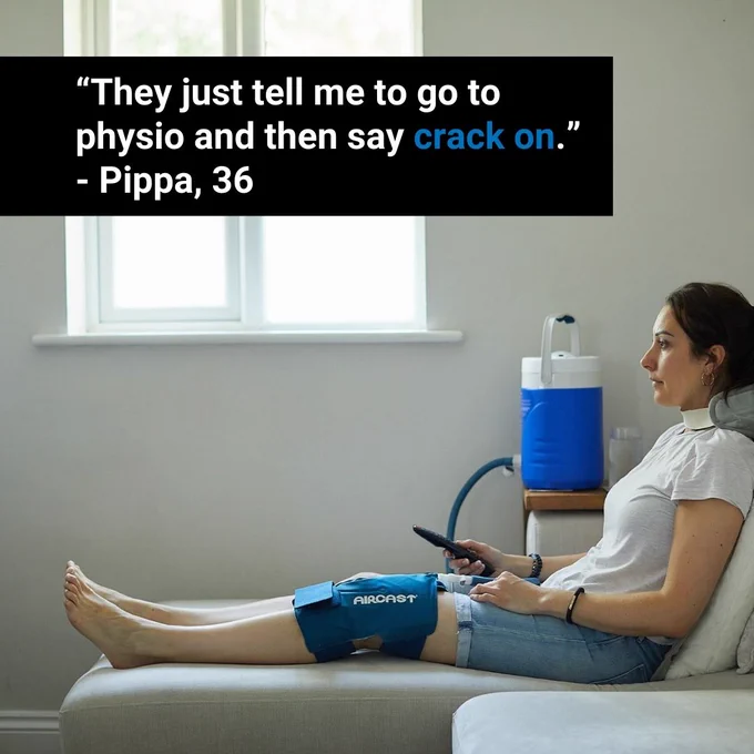 An image of an individual seated on a gray couch using a blue medical device on their leg, likely for physical therapy. They hold a remote control and appear focused on something out of view. Above them, text in quotation marks reads: “They just tell me to go to physio and then say crack on.” - Pippa, 36. The scene is set against a simple room with a plain white wall.