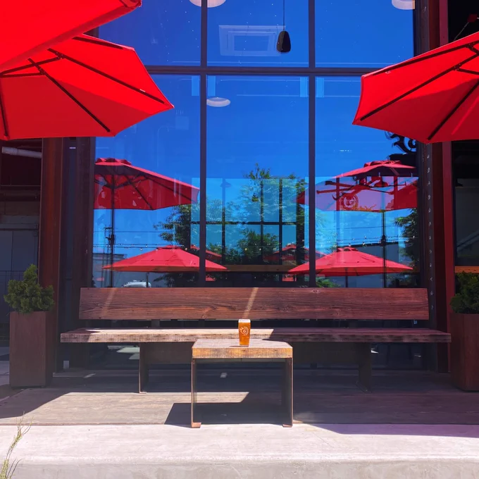a photo of our beer garden featuring our new sun umbrellas in a vibrant shade of red, reflected in the windows to create the illusion of even more umbrellas. A pint of beer sits on a table but it is not the focus of the photo.