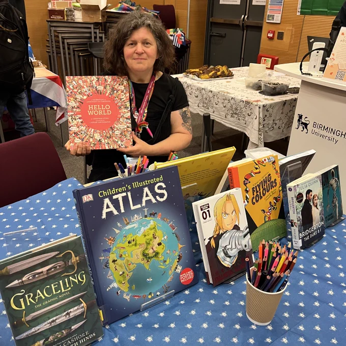 One of our BCU librarians is sat at a stall surrounded by books and art materials for badge making.