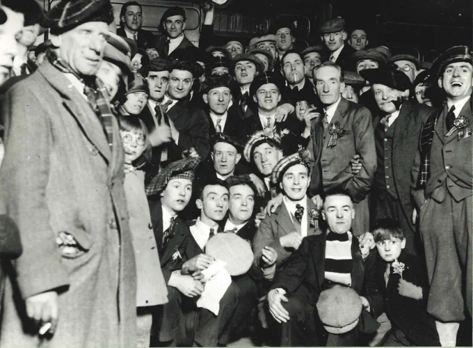 large group of men and boys, many wearing tartan bunnets and scarves photographed on their way to a football match