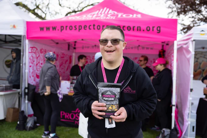 EJ smiles in front of the Prospector Popcorn tent while holding a bag of gourmet popcorn.