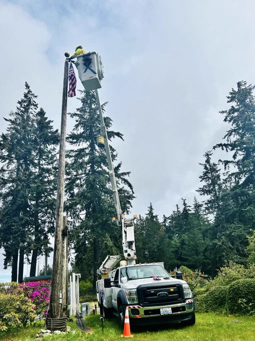 A Comcast Technician replaces an American flag at the top of a flag pole with an Xfinity truck. 