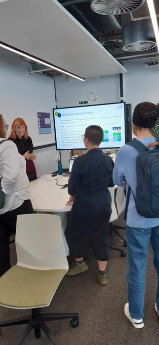 Helen is standing in front of her presentation whilst three people listen. They have their backs to the camera.