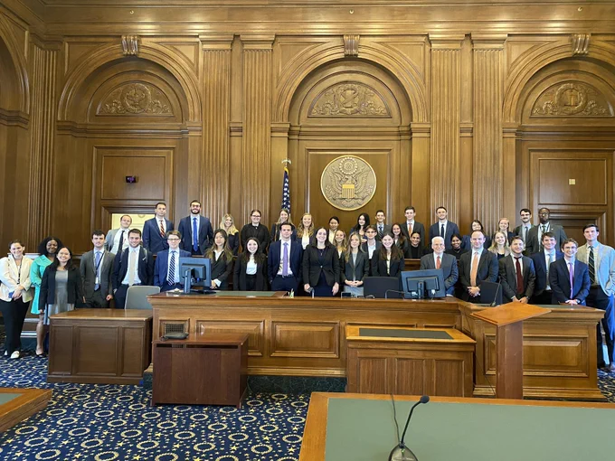 Large group of interns pose for a photo in a courtroom.