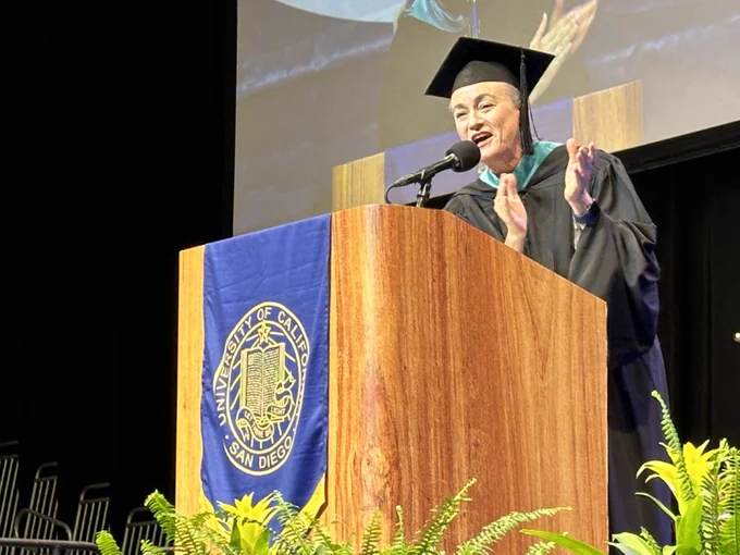 Ambassador Liliana Ferrer-Silva claps at a wooden podium to congratulate GPS graduates.