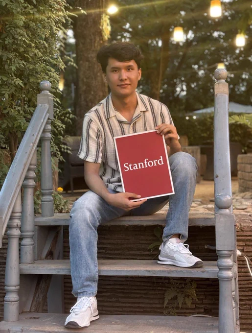Morteza sat on some steps holding a paper that says ‘Stanford’